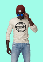 Load image into Gallery viewer, Man wearing a cream-colored "Every Internal Things" long sleeve t-shirt with bold black circular logo, blue jeans, red beanie, and blue sunglasses, standing against a teal background.