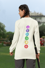 Load image into Gallery viewer, Woman standing outdoors wearing an ivory long-sleeve shirt with a vertical row of colorful chakra symbols printed on the back.