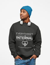 Load image into Gallery viewer, Man wearing a black unisex sweatshirt with “Everything’s Internal” logo, blue beanie, and white headphones, standing against a light gray background.
