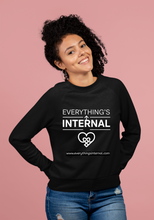 Load image into Gallery viewer, Woman smiling and wearing a black unisex sweatshirt with “Everything’s Internal” logo, standing against a pink background.
