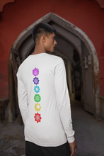 Load image into Gallery viewer, Man standing in front of an archway wearing a white long-sleeve shirt with a vertical row of colorful chakra symbols printed on the back.
