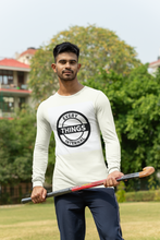 Load image into Gallery viewer, Man standing outdoors holding a hockey stick, wearing a white long-sleeve shirt with the &quot;Every Things Internal&quot; black graphic logo on the front.
