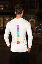 Load image into Gallery viewer, Man standing outdoors at night wearing a white long-sleeve shirt with colorful chakra symbols vertically aligned on the back.
